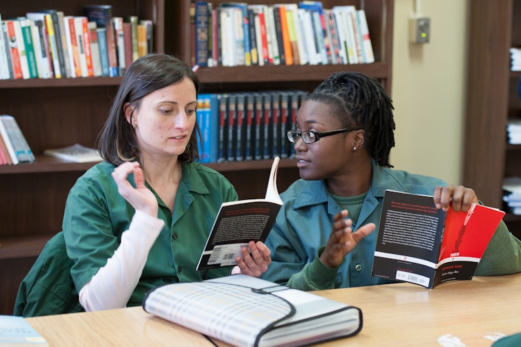 Two people discuss a book as part of the Bard Prison Initiative at a women’s prison in Bedford Hills, New York, on March 24, 2015. Photo credit: © China Jorrin for the Bard Prison Initiative Two women holding books at a table