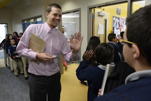 A middle school teacher greets students at the door of his classroom in Denver, Colorado, on October 15, 2014. Photo credit: © Andy Cross/Denver Post/Getty Teacher with his palm up in front of a line of students
