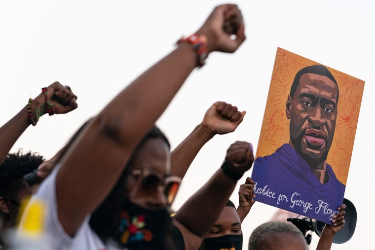 People raise their fists following the guilty verdict in the trial of the Minneapolis police officer who killed George Floyd on April 20, 2021, in Atlanta, Georgia. Photo credit: © Elijah Nouvelage/AFP/Getty People raising their fists with a drawing of George Floyd in the background