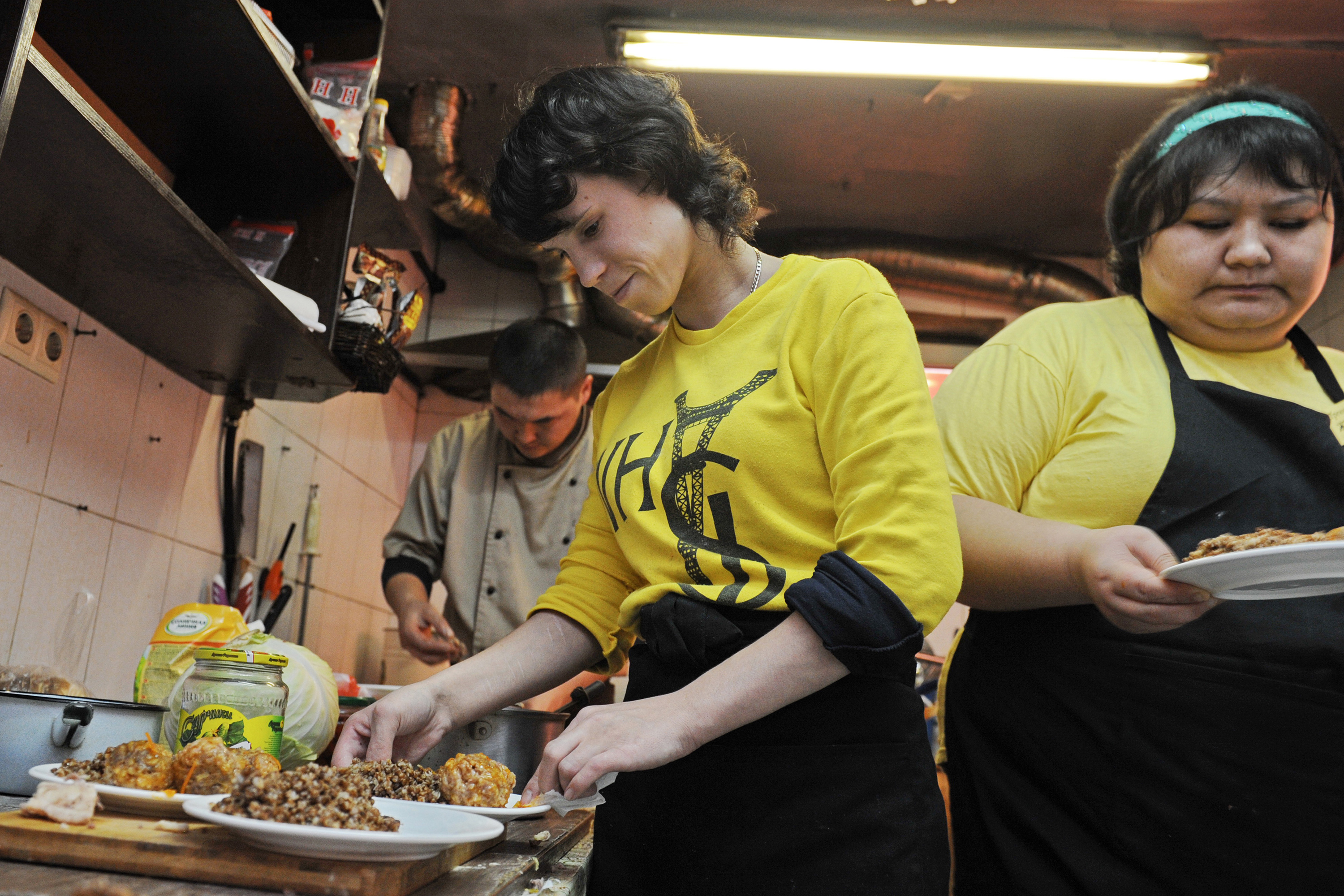 People in yellow shirts create plates of regional cuisine in the kitchen of a café.