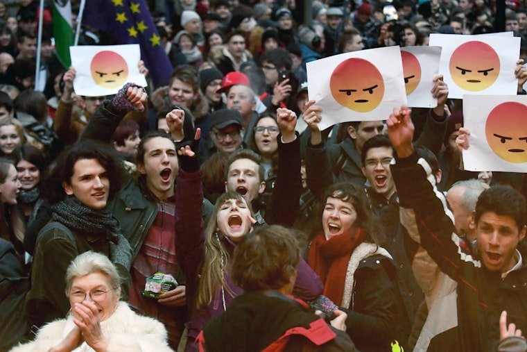 Students in Budapest, Hungary, hold up signs showing an angry emoticon during protests against the government's education policy on January 19, 2018. Photo credit: © Attila Kisbenedek/AFP/Getty A crowd of young people stand outside in the cold while raising signs featuring an illustrated cartoon face that is supposed to represent anger.