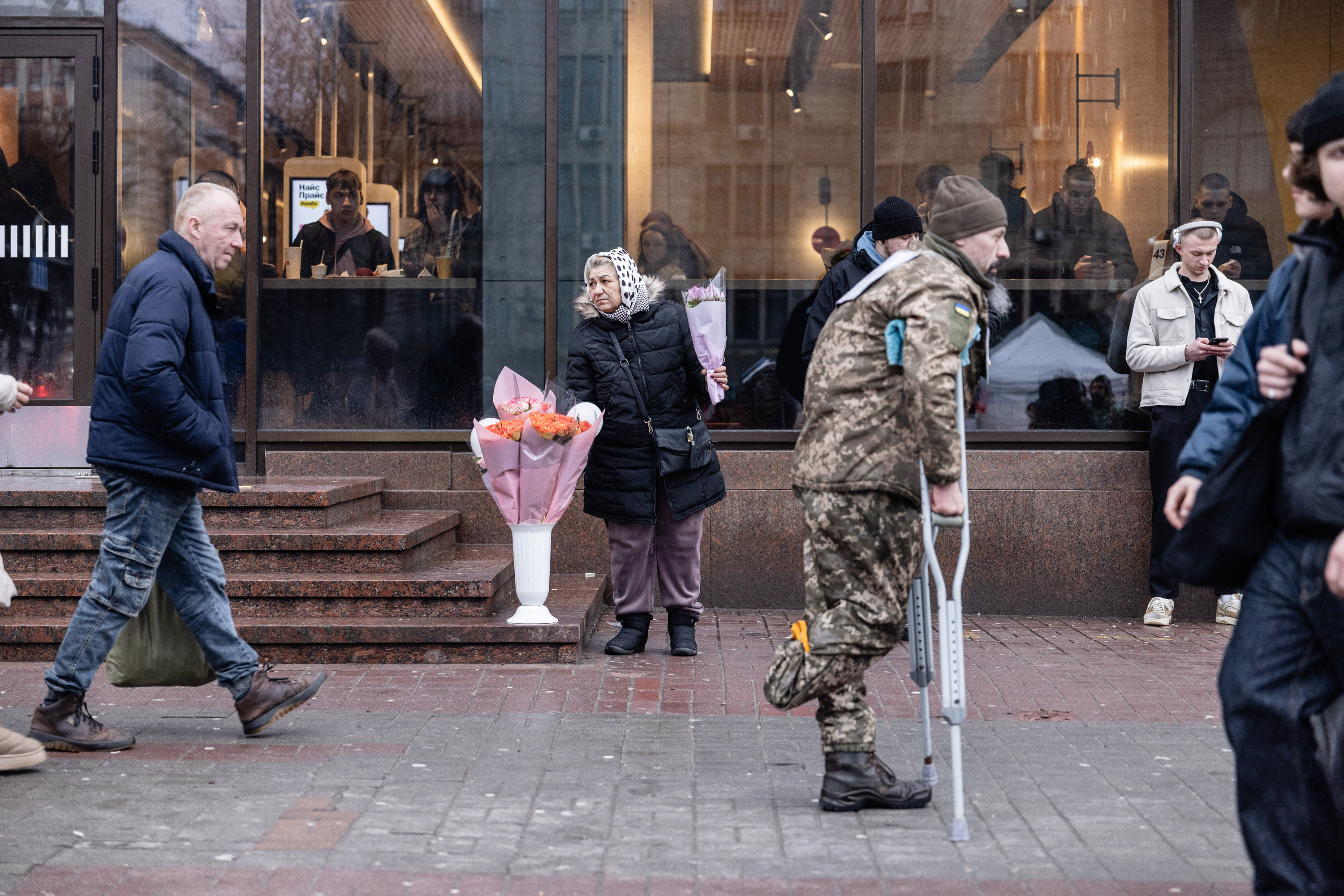 A man in military fatigues walking on crutches on a busy street