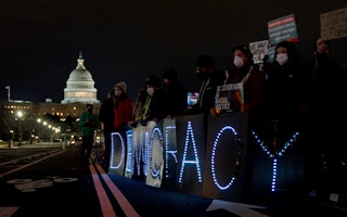 People hold LED signs near the US Capitol at night.