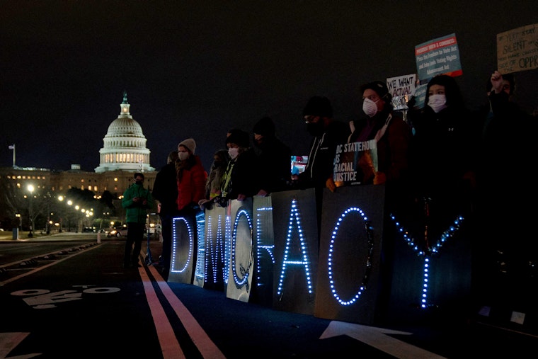 People hold LED signs near the US Capitol at night.