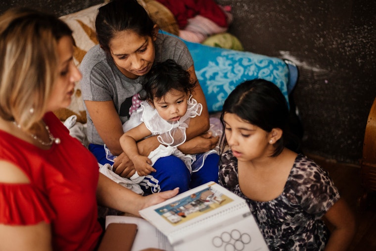 A woman reads an education pamphlet to a woman and her two children.
