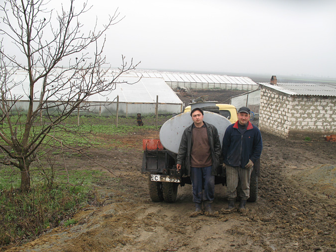 Two men stand in front of a truck on a farm