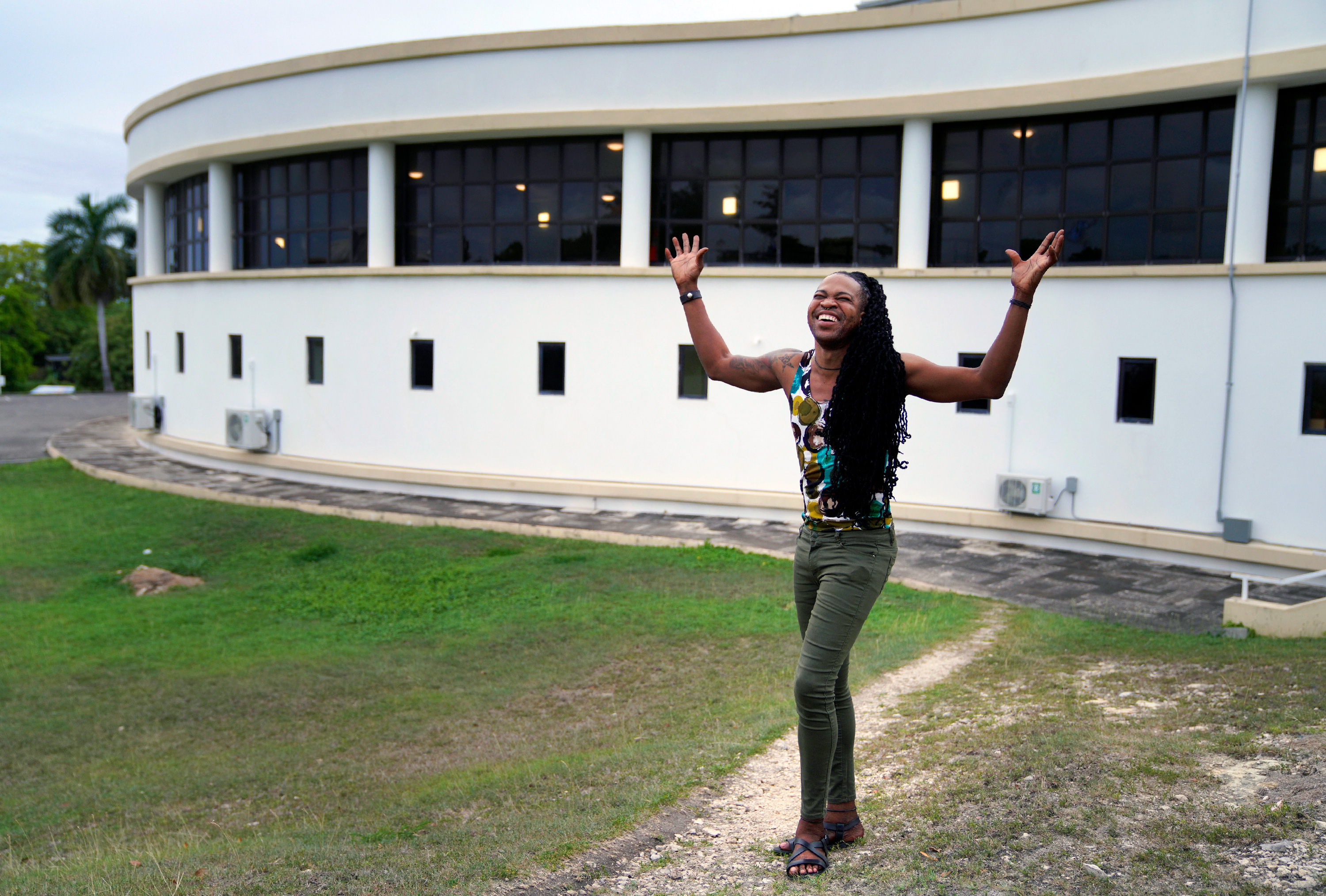 A person stands in front of a building with their hands in the air