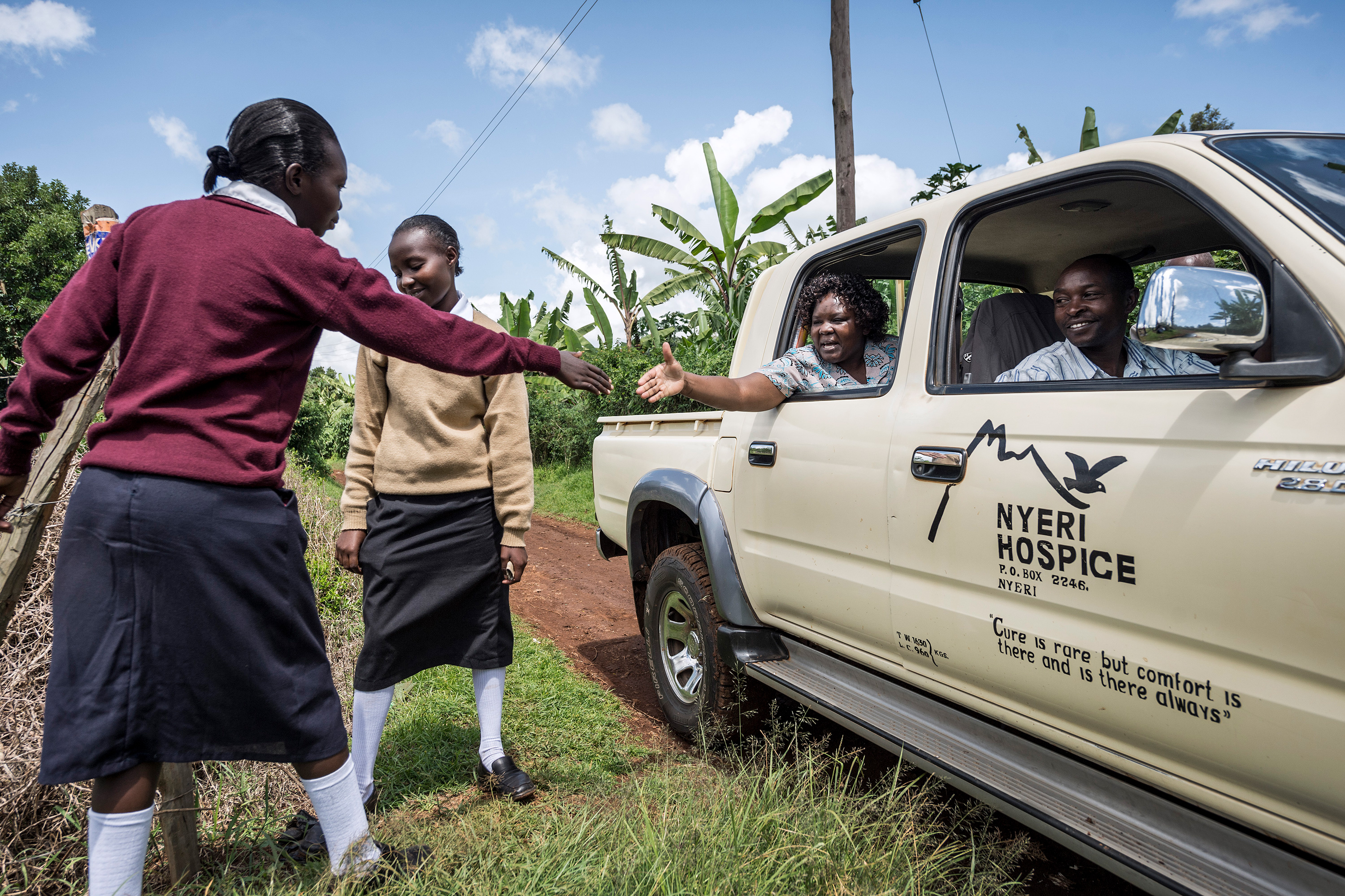 A woman reaches out of the window of a pickup truck to shake hands with a girl.