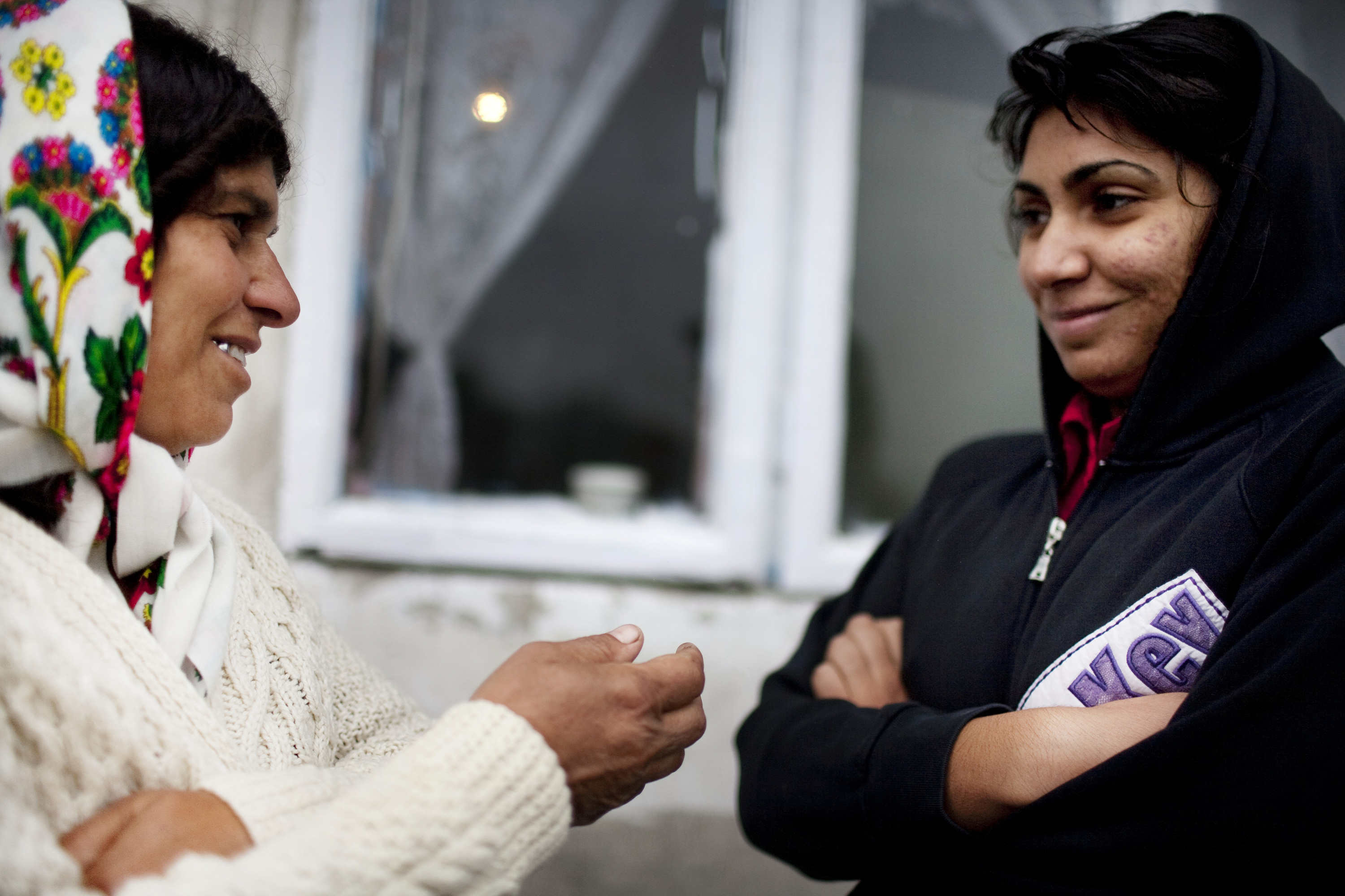 Two women speak outside of a house.