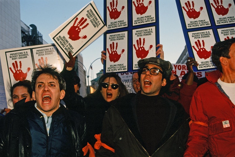 AIDS activists, including Daniel Wolfe (right), protest in New York City in 1996. Photo credit: © Allan Clear Protestors with signs and red arm bands marching in the street