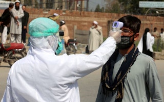 A person wearing protective gear points a thermometer at a man