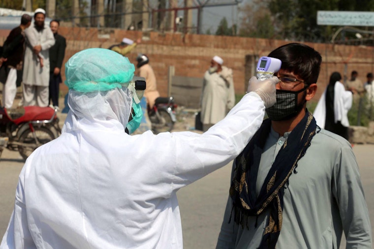 A man in Peshawar, Pakistan, has his temperature taken, on March 18, 2020. Photo credit: © PPI/Zuma/Newscom A person wearing protective gear points a thermometer at a man