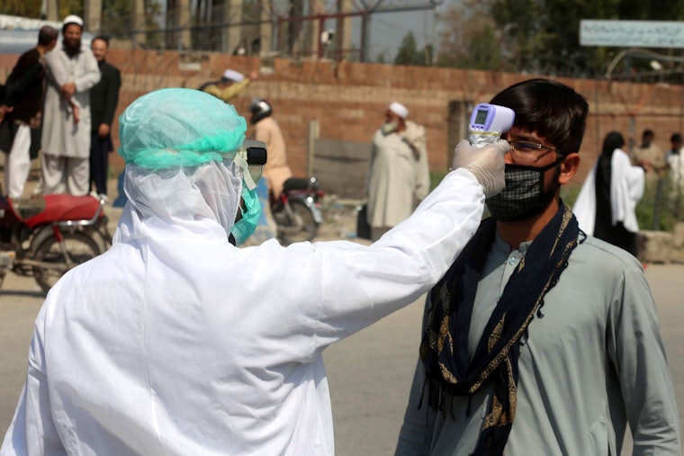 A person wearing protective gear points a thermometer at a man