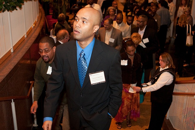 Anthony Simmons in suit, walking up stairs in crowded room