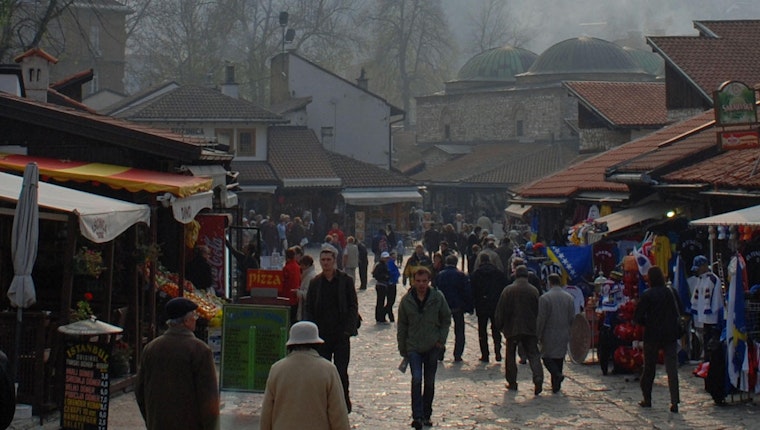 Still image from The Siege of Sarajevo and the Dream of Open Society. When the city Sarajevo was under siege during the war in Bosnia, the very idea of open society was under assault. Working together with Bosnians—from artists to engineers—George Soros supported efforts to ensure the survival of the city and its culture. In a time of fear and darkness, the human spirit proved invincible. A crowd of people walking in a market