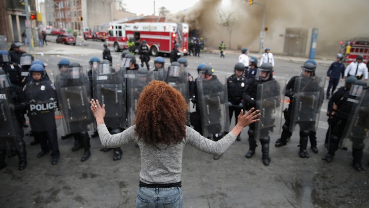 Still photo from “Baltimore Rising: Policing After Freddie Gray.” There is a segment of the population in the United States—mostly poor, and people of color—who have been living on the margins of our society for too long. And they have been victimized by an aggressive and unfair criminal justice system, the face of which is the police, who regrettably harass and threaten poor people and people of color every day. Photo credit: © Chip Somodevilla/Getty Woman in front of police