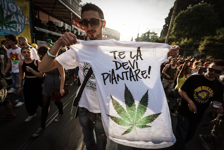 A man holding up a t-shirt printed with a marijuana leaf