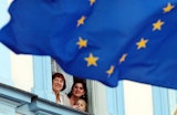People looking out a window behind a European Union flag
