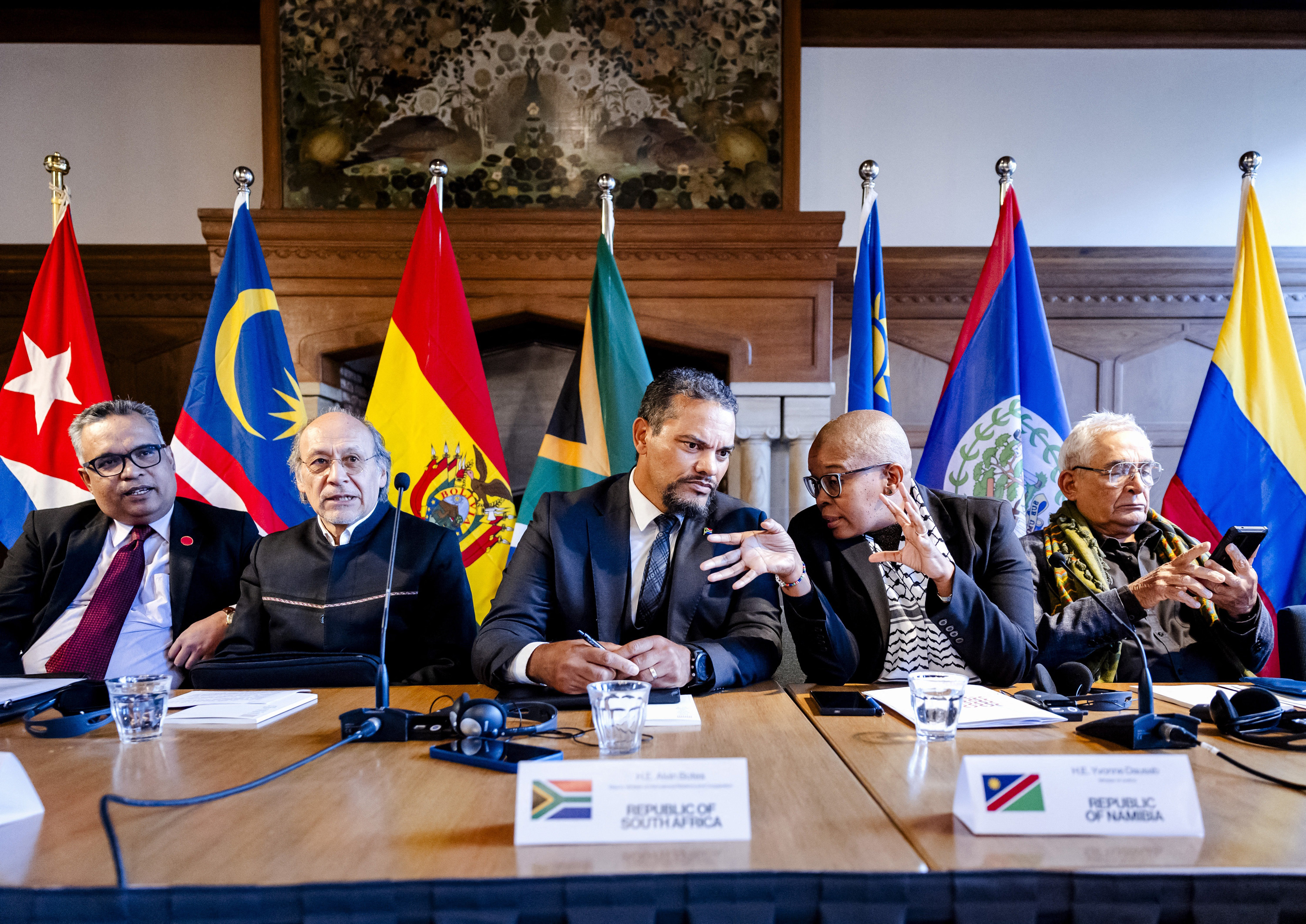 A group of people sit at a meeting table with flags behind them