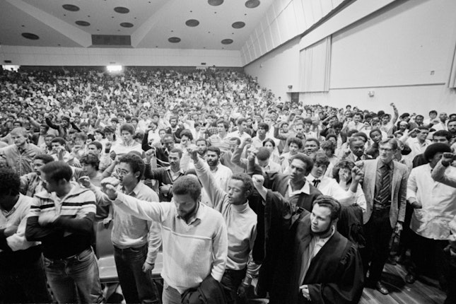 A hall full of students with their fists in the air
