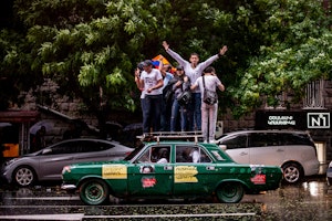A group of people standing on top of a green car