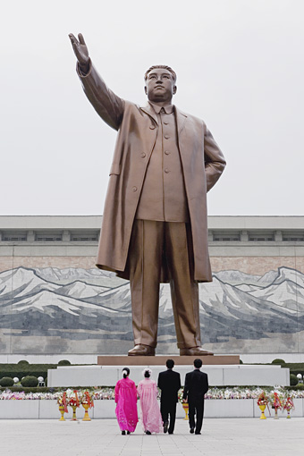 People standing in front large statue of Kim Il Sung