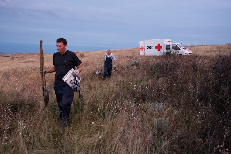 Two people walking through a field with digging equipment