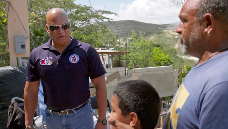 Still image from “Mayors to the Rescue for Puerto Rico.” With government relief operations falling short, a group of mayors are joining together to help Puerto Rico recover from Hurricane Maria. Three people standing in the ruins of a house