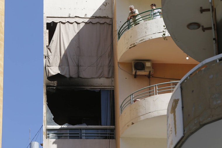 Two people stand on the balcony of an apartment building.