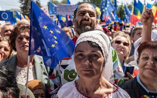 A woman stands in front of a crowd of people holding European Union flags.