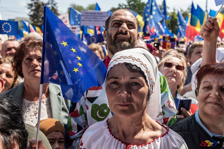 A woman stands in front of a crowd of people holding European Union flags.