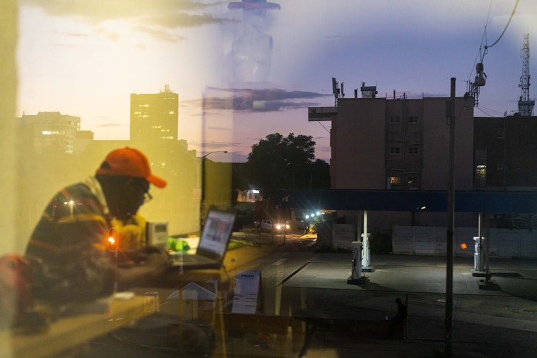 A person working on a laptop seen through window glass with reflections