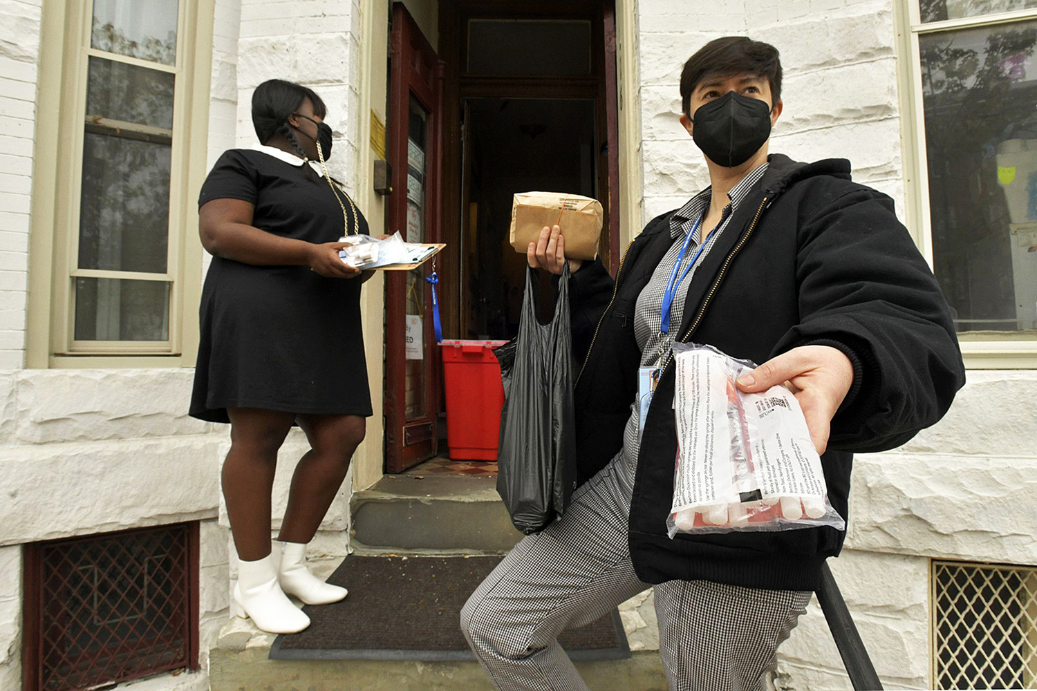 Two people holding supplies on the stoop of a house.