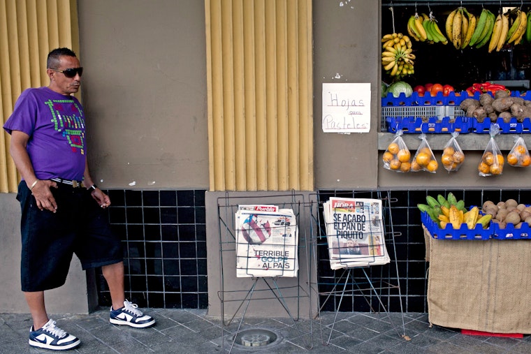 In the city of Ponce, Puerto Rico, a man stands next to newspapers displaying stories about the country’s credit rating downgrade in February 2014. Photo credit: © Alvin Baez/Newscom Man at a fruit stand