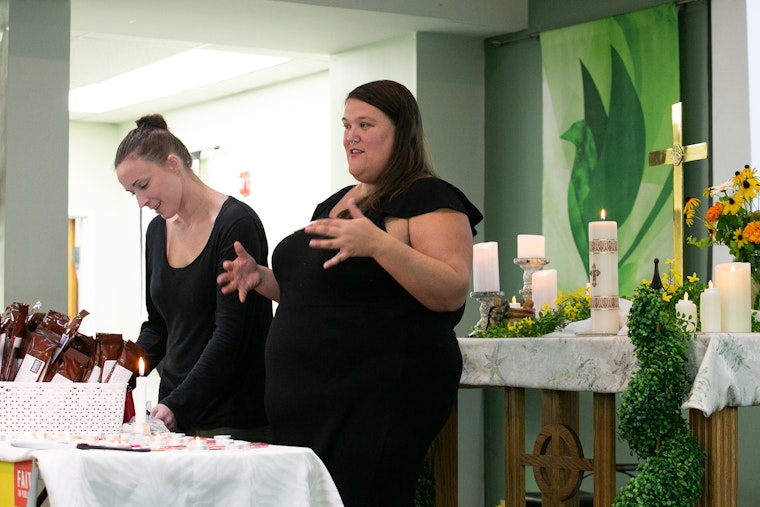 A pastor leads a church service to provide healing and distribute naloxone, the overdose reversal medicine, at the United Methodist Church for All People in Columbus, Ohio, on September 5, 2019. Photo credit: Kristen Lieb/Redux for the Open Society Foundations Two women standing at a table with candles and a cross in the background