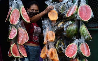 A fruit vendor standing next to bags of sliced fruit