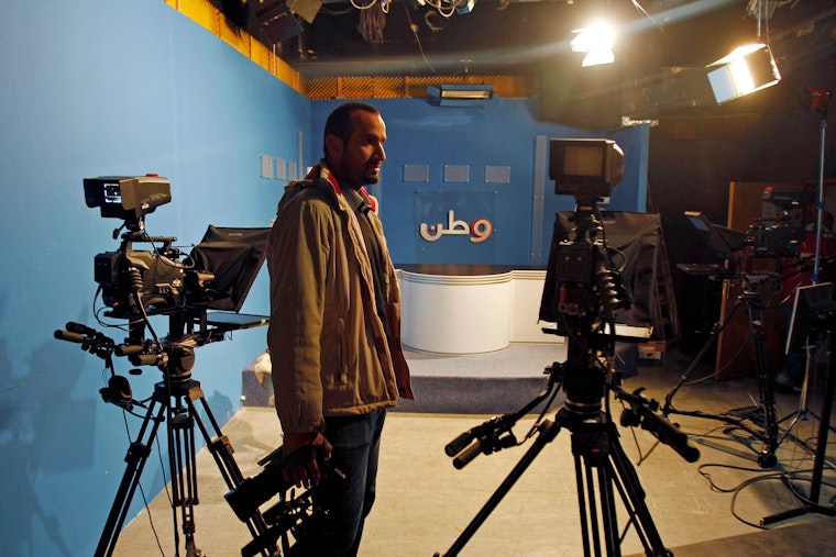 A man stands in a television studio holding a camera