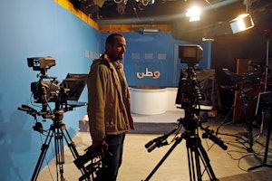 A man stands in a television studio holding a camera