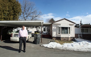 A man stands in front of his car and mobile home.