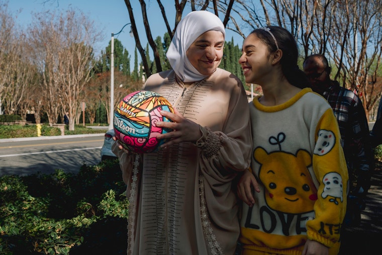 A Syrian refugee family walks near their apartment in Anaheim, California, on December 15, 2024. Photo credit: © Mark Abramson/NYTimes/Redux A woman in a hijab holding a basketball walking outside next to a girl wearing a sweater that says, "Love"