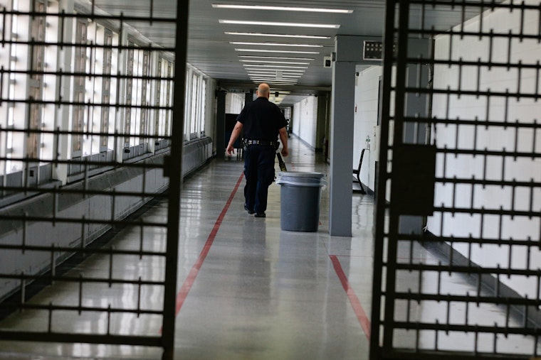 A Rikers Island juvenile detention facility officer walks down a hallway of the jail. Photo credit: © Julie Jacobson/AP Photo A man walking in a corridor.