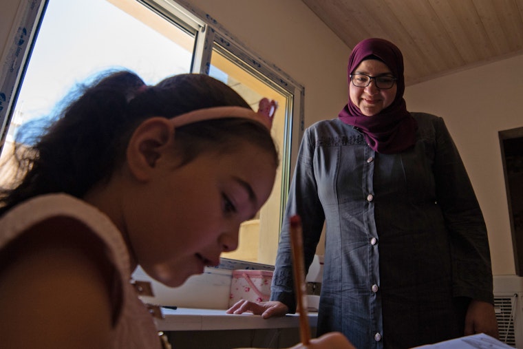 Ghada, a refugee from Syria who takes on many leadership roles in her community, works with a young student in Bekaa, Lebanon, on August 20, 2020. © Ali Khedr for the Institute of International Education A woman speaks to a girl at a desk