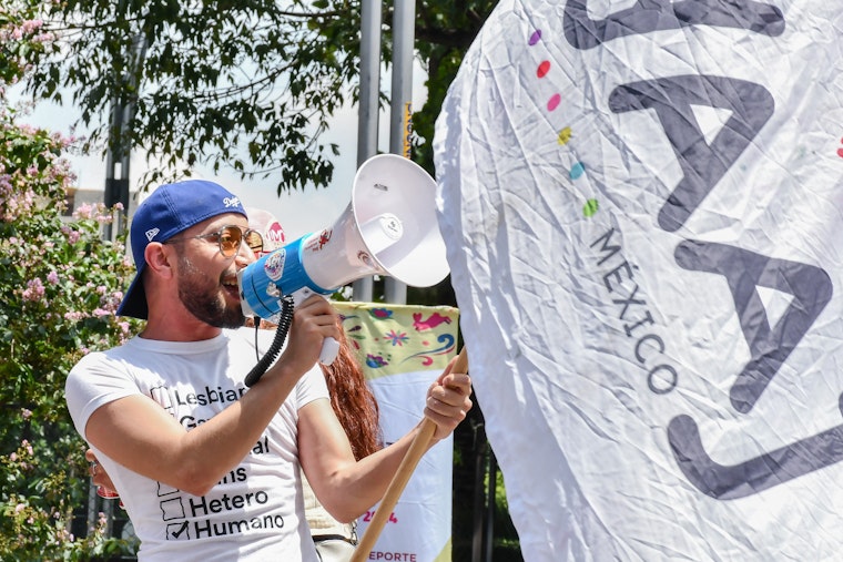 Iván Tagle speaks through a megaphone during the Mexico City Pride march on June 29, 2024.
© Sylvia Cortés for Yaaj México A man stands with a megaphone and waves a flag