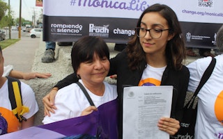 Two women stand next to each other holding a piece of paper