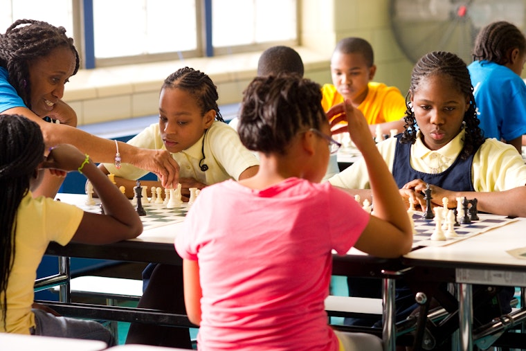 Students play chess in pairs in a cafeteria.