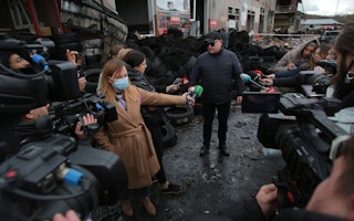 Video journalists and reporters around a man with car tires in the background