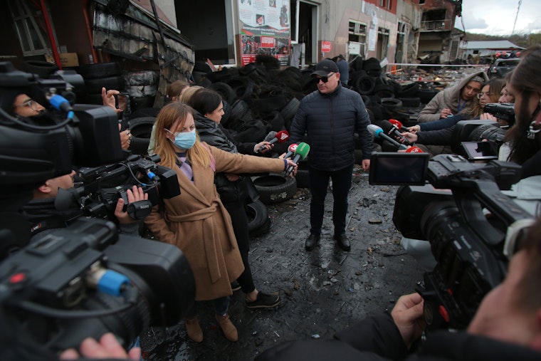 Video journalists and reporters around a man with car tires in the background