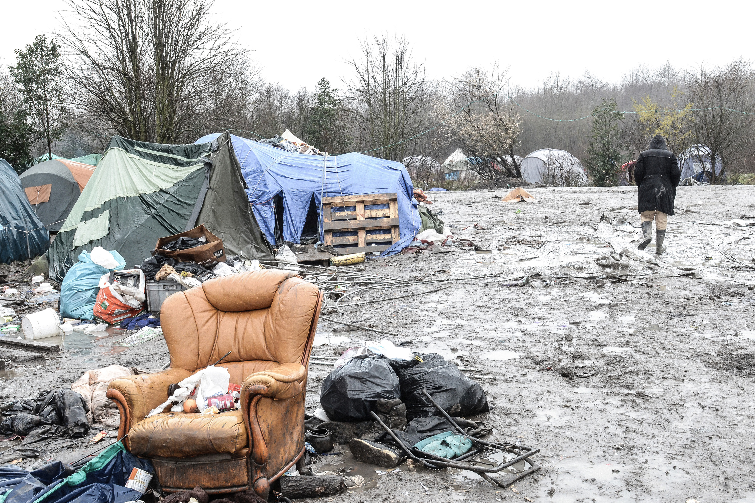 A woman walks through mud toward camping tents