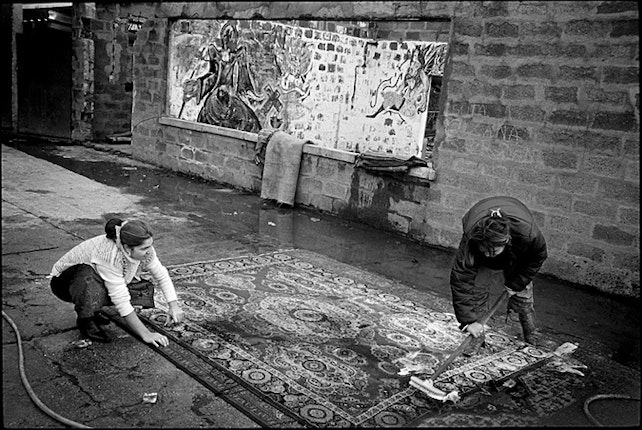Two women cleaning a rug outdoors