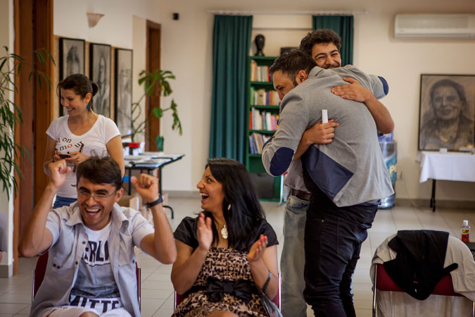 Two men hugging in a classroom while others cheer.